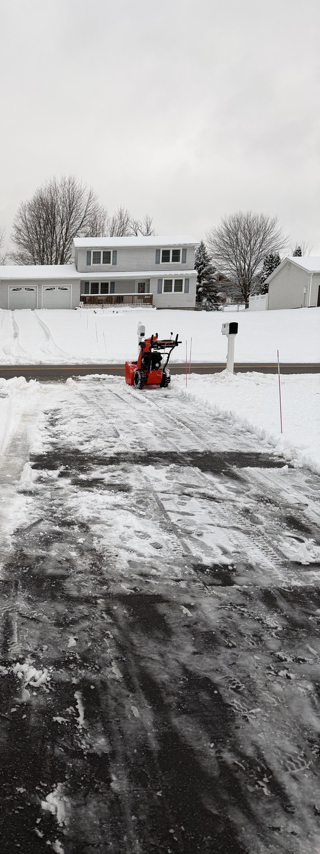 A driveway cleared of snow in daylight, the red snow blower parked at the street