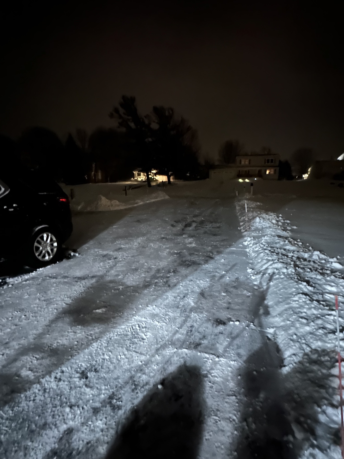 A driveway cleared of snow at night, lit up against the dark street